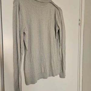 Turkos silkesmixad polotröja  - En stilren ljust turkos polotröja i storlek L med hög polokrage. Tillverkad i en lyxig mix av silke, nylon och kashmir som ger en mjuk och skön känsla. Två små ihopsydda hål på kragen som knappt syns