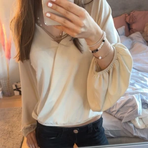 Beige omlottblus med ballongärmar - Säljer en beige omlottblus med v-ringning och långa ballongärmar med resår vid handlederna. Blusen har en avslappnad passform och är perfekt för dig som gillar en stilren och trendig look. Materialet känns mjukt och lätt mot huden. Hör av er vid några frågor! Accepterar dem flesta buden! 💕