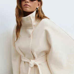Beige capejacka med bälte från Gina Tricot - Säljer en beige capejacka från Gina Tricot med hög krage, knappar och knytskärp i midjan. Jackan har vida ärmar och en snygg, oversized siluett. Perfekt för dig som vill ha en stilren och trendig look till höst och vår. Trendig jacka som tog slut snabbt. Jackan har aldrig används och lappen sitter kvar. Hör av dig vid frågor!💗