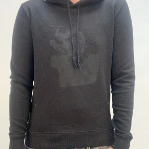 Svart hoodie med snörning - Svart hoodie med klassisk huva och snörning framtill. Tröjan har långärmad passform och ribbade muddar vid ärmslut och nederkant. Enkel och stilren design som passar till det mesta.