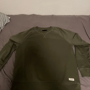 Mörkgrön sweatshirt från 157, stl S - En stilren mörkgrön sweatshirt från 157 i storlek S. Tröjan har rund halsringning, ribbade muddar och en liten patch nertill. Perfekt basic med relaxed fit och långa ärmar, tillverkad i mjuk bomullsmix. Knappt använd, inga defekter eller sådant.