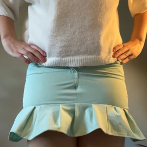 Mintgrön kortkjol med volang - Supersöt mintgrön/turkos kortkjol med volangkant längst ner. Kjolen har en tight passform och är tillverkad i ett mjukt bomullsmaterial som sitter skönt mot kroppen. Perfekt för dig som gillar en fräsch och lekfull stil med extra detaljer.