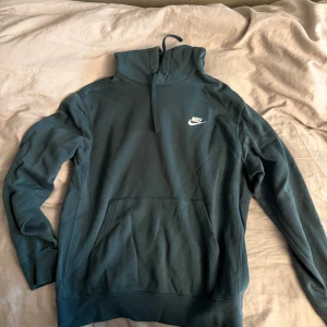 Blå hoodie från Nike - Snygg blå hoodie från Nike med vit logga på bröstet. Tröjan har huva med snörning, stor magficka och är långärmad. Mjuk insida i fleece som gör den extra skön. Perfekt för chill eller träning, passar dig som gillar sportig stil.