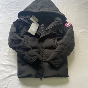  Canada Goose vinterjacka - Svart dunjacka från Canada Goose i storlek XS. Jackan har huva, klassisk patch på ärmen och dragkedja med tryckknappar. Fodrad och quiltad för extra värme, perfekt för kalla dagar. Snygg och stilren design med raka linjer och diskreta detaljer. Kommer med fur 
