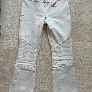 Vita täckbyxor från Cross Sportswear - Vita täckbyxor från Cross Sportswear med snygga quiltade detaljer över knäna. Byxorna är vattentäta, har två svarta knappar i midjan på utsidan men tre på insidan och är tillverkade i ett slitstarkt syntetmaterial. Perfekta för vinterns alla äventyr i backen.