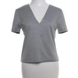 Grå v-ringad topp från Zara Trafaluc - Snygg grå topp från Zara Trafaluc med v-ringad hals och korta ärmar. Modellen är enkel och stilren, perfekt för dig som gillar en clean look. Materialet är mjukt och känns skönt mot huden. Passformen är normal och toppen är lätt att matcha med dina favoritjeans.