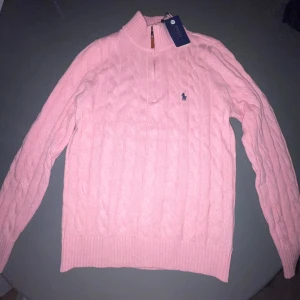 Rosa stickad polotröja från Polo Ralph Lauren - Supersnygg rosa polotröja från Polo Ralph Lauren med klassisk kabelstickning och liten broderad logga på bröstet. Tröjan har half zip-dragkedja vid halsen och är långärmad med ribbade muddar. Perfekt för lager-på-lager och chill stil.