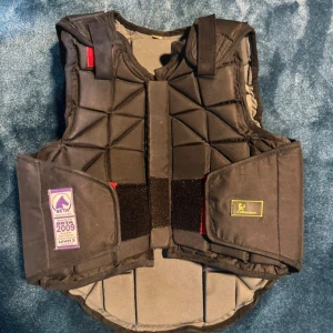 Svart skyddsväst från Globus Sport CXL - Skyddsväst i svart från Globus Sport, storlek CXL. Västen har quiltad design med triangulära paneler och bred kardborrestängning framtill. Märkt med BETA Level 3 för extra säkerhet vid ridning. Perfekt för dig som vill ha både stil och skydd i stallet. Aldrig varit med om något fall