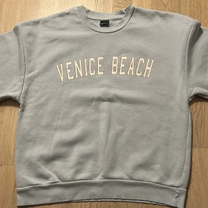 Ljusblå sweatshirt från Gina Tricot nyskick - Säljer en ljusgrå sweatshirt från Gina Tricot med trycket 'Venice Beach' i vitt framtill (aldrig använt)! Tröjan har rund halsringning, ribbade muddar och en relaxed passform. 