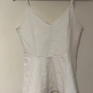 Vit topp  - Säljer en stilren vit topp från Gina Tricot med smala axelband och v-ringning. Toppen har figurnära passform och är tillverkad i mjuk bomullsmix, perfekt att matcha med jeans eller kjol för en fräsch look. Använd enstaka gånger. Har en liten fläck på högersidan vid bandet som säkert går bort i tvätten💞