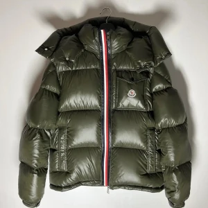  Moncler Maya vinter jacka, NFC - Snygg mörkgrön pufferjacka från Moncler med ikonisk logga på bröstet och cool randig dragkedja. Jackan har hög krage, stora vadderade partier och praktiska fickor. Perfekt för kalla dagar när du vill hålla stilen.