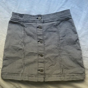 Rutig kortkjol med knappar från H&M🍂 - 🍂Supersnygg kortkjol från H&M i svartvitt rutigt mönster. Kjolen har hög midja och dekorativa silverfärgade knappar framtill. Perfekt för dig som gillar klassisk stil med en twist. Tillverkad i bomull för en skön känsla.🍂