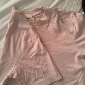 Ljusrosa t-shirt från Gina Tricot - En basic ljusrosa t-shirt från Gina Tricot, basically basics-kollektionen. T-shirten har rund halsringning med ribbad kant och korta ärmar. Perfekt för en clean och enkel look. Tillverkad i mjuk bomull för skön känsla hela dagen.