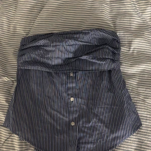 Randiga blå shorts från FB Sister - Säljer en blå och vita randig tub-topp från FB Sister i storlek XS.  lite skjortlik look. Perfekta för dig som gillar en chill men ändå stilren vibe. Materialet känns lätt och passar bra till varmare dagar.