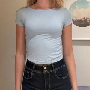 Ljusblå topp med lite öppen rygg - En enkel och fräsch ljusblå croppad topp med rund halsringning och korta ärmar samt lite öppen rygg. Toppen har en tight passform och är tillverkad i mjuk bomull, perfekt till jeans eller kjol för en clean look. Köpt på barnavdelningen på lager 157 i storlek 146, sitter som xs/s. Aldrig använd!! 