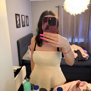 Krämvit bandeau tubtopp - Säljer en krämvit bandeau tubtopp med utsvängd nederdel. Toppen är ärmlös och har en mjuk, lätt rynkad struktur som ger en söt och feminin look. Perfekt för varma dagar och enkel att styla med jeans eller kjol.