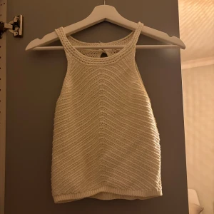 Vit stickad linnetopp med nyckelhålsdetalj - Säljer en vit stickad linnetopp och snyggt virkat mönster. Toppen har ett nyckelhålsformat spänne i nacken och är ärmlös. Perfekt för varma dagar och enkel att styla till jeans eller kjol.