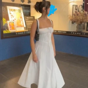 Vit långklänning med snörning - Superfin vit långklänning med breda axelband, snörning både fram och bak samt slits framtill. Klänningen har en feminin siluett och är gjord i ett lätt material som ger ett snyggt fall. Perfekt för sommarens alla tillfällen!