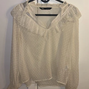 Blus med volang  - Supersöt vit blus från Zara med diskret prickigt mönster, volangkrage och långa ärmar med smock vid handlederna. 
