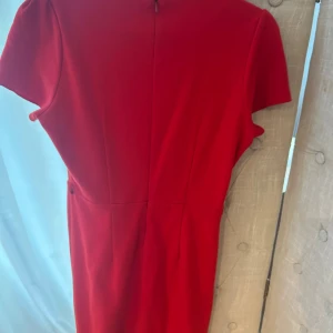 Röd kortärmad klänning från Mango - Snygg röd klänning från Mango med korta ärmar och rund halsringning. Modellen är figurnära upptill och har en lätt utställd kjol. Dragkedja bak för enkel påklädning. Perfekt för dig som vill sticka ut med en klassisk och stilren look.