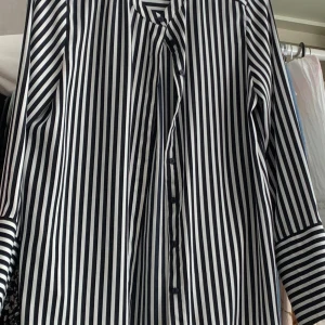 Svartvit randig skjorta med knappar - Snygg skjorta med svarta och vita vertikala ränder och knäppning framtill. Skjortan har lång ärm och klassisk krage, perfekt för en stilren look. Materialet känns mjukt och följsamt mot huden.