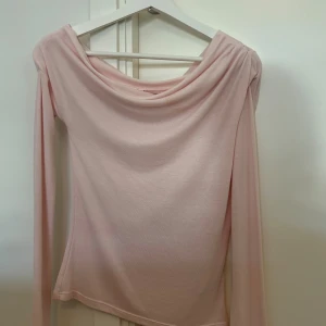 Ljusrosa långärmad topp från Nelly - Säljer en ljusrosa långärmad topp från Nelly med snygg draperad halsringning. Toppen har en slim passform och är tillverkad i mjukt, stretchigt material som sitter skönt på kroppen. Perfekt för dig som gillar stilrena och feminina plagg. Helt ny och aldrig använd. 