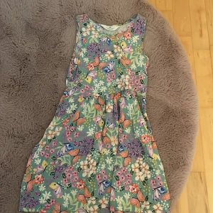 Blommig ärmlös klänning H&M 134/140 - Superfin ärmlös klänning från H&M i storlek 134/140. Klänningen har en ljusgrön bas med färgglatt blommönster i rosa, lila, vitt och orange samt fjärilar.🦋 