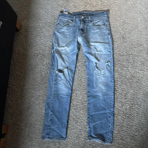 Levis 511 ljusblå slitna jeans W30 L32 - Ljusblå Levis 511 jeans med slitningar och hål på båda knäna. Klassisk femficksmodell med raka ben och normal passform. Jeansen har en snygg tvättad look och är tillverkade i bomull. Perfekta för en avslappnad streetstil.