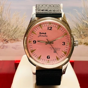 HMT Janata Automatic Herr klocka med rosa urtavla - Snygg HMT Janata klocka med rund boett i silverfärgad metall och en stilren rosa urtavla. Klockan har svarta siffror, silverfärgade visare och svart textilband. En klassisk och unik accessoar som sticker ut med sin färg och retrostil.Säljes i fungerande skick enligt bilderna!