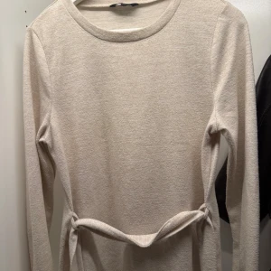 Beige långärmad tröja Happy Holly - Stilren beige tröja från Happy Holly, har ett knytband i midjan som ger en snygg siluett. Perfekt för dig som gillar enkel och tidlös design.