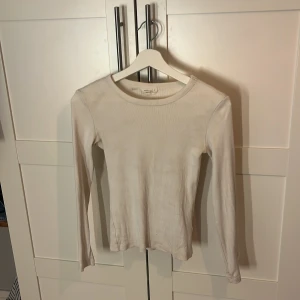 Vit ribbad långärmad tröja Gina Tricot - En basic vit långärmad tröja från Gina Tricot, ribbad och i figurnära modell. Perfekt att styla med jeans eller kjol. Mjuk och stretchig bomullskvalitet, rund halsringning och enkel design.