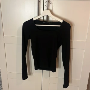 Svart långärmad topp från 157 - Svart långärmad topp från 157 med fyrkantig halsringning. Modellen är slim och har en stilren, enkel design utan mönster eller detaljer. Materialet känns mjukt och stretchigt, perfekt för dig som gillar minimalistiska plagg med snygg passform.