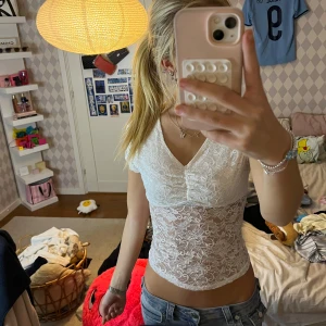 Vit spetsblus med v-ringning - Säljer en vit, genomskinlig spetsblus med v-ringad hals och korta ärmar. Blusen är croppad och har ett fint blommigt spetsmönster över hela plagget. Perfekt för dig som gillar romantisk och feminin stil.