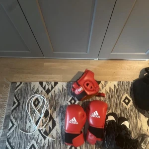 Röda boxningshandskar Adidas 10oz - KOM OCH HÄMTA KNIVSTA (Uppsala) Säljer ett par röda boxningshandskar från Adidas, 10oz, med AIBA-godkännande. Handskarna är i skinn och har klassisk boxningsform med kardborreknäppning. Perfekta för träning eller match. Snygg design med vit Adidas-logga på ovansidan.