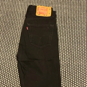 Svarta Levi's 501 jeans  - Svarta Levi's 501 jeans med klassisk straight fit och fem fickor. Byxorna har den ikoniska läderpatchen bak och silverfärgade nitar framtill. Jeansen är tillverkade i slitstarkt bomullsmaterial och har knappgylf. Perfekt för dig som gillar tidlös stil.