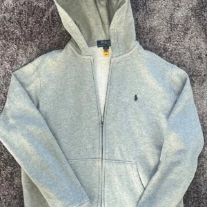 Ralph Lauren hoodie  - Säljer en stilren Ralph Lauren Zipp upp i färgen grå. Storleken är L(14-16) och skicket är som nytt. Passar till både damer och herrar. Vid frågor är det självklart bara att höra av dig😊