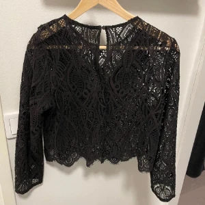 Svart spetsblus med volang från Zara - Supersnygg svart blus i spets från Zara med lång ärm och volangdetalj framtill. Den är i storlek M men sitter som en S! 