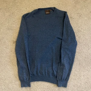 Blå rundhalsad tröja Oscar Jacobson - Snygg blå rundhalsad tröja från Oscar Jacobson i mjuk ull. Klassisk modell med ribbade muddar vid ärmslut och nederkant. Perfekt för dig som gillar stilrena och bekväma plagg. Tillverkad i Italien.