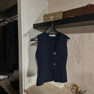 Mörkblå väst från Zara med guldknappar - Stilren mörkblå väst från Zara med v-ringning och två snygga guldknappar framtill. 