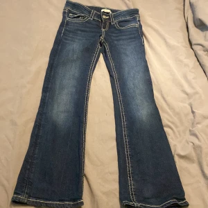 Blå bootcut jeans från Gina Tricot low rised - Snygga mörkblå jeans från Gina Tricot i storlek 140 med bootcut passform. Klassisk femficksdesign, kontrastsömmar och knappstängning fram. Bakfickorna har lock och knappdetalj. Perfekta för dig som gillar retrovibbar och markerade sömmar. 
