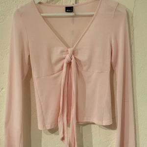 Ljusrosa långärmad topp med knyt från Ginatricot  - Supersöt ljusrosa topp från Gina Tricot med lång ärm och djup v-ringning. Toppen har en snygg knyt-detalj framtill som ger en feminin och trendig look. Använd några gånger, lite nopprig!🩷köpt för 300 kr. 