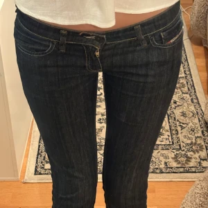 Mörkblå Diesel LIV jeans W28 L32 - Snygga mörkblå jeans från Diesel, modell LIV. Klassisk femficksdesign med kontrastsömmar och väldigt låg midja. Jeansen har raka ben och är tillverkade i slitstarkt denimtyg. Perfekta för dig som gillar en tidlös och clean look.