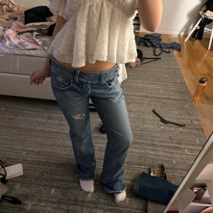 Lågmidjade blå bootcut jeans diesel - Säljer ett par blå jeans med låg midja och bootcut passform. Jeansen har slitna detaljer och flera knappar i midjan för en cool look. Klassisk femficksmodell i denim med ljus tvätt och råa kanter vid benslut. Saknas en knapp på insidan (se bild!) märks dock inte. 