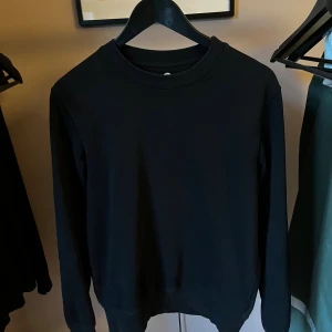 Tröja från Cubus  - En stilren svart sweatshirt med rund hals och långa ärmar. Tröjan är enkel och passar perfekt till jeans eller joggers. Tillverkad i mjuk bomull för en skön känsla hela dagen. Strl S