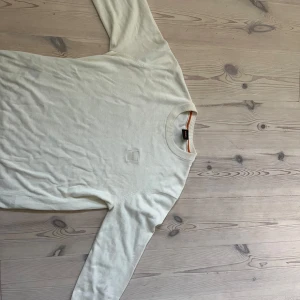 BOSS tröja - Säljer en stilren biege långärmad tröja från BOSS med broderad logotyp på bröstet. Tröjan har rund halsringning och är tillverkad i mjuk bomull, perfekt för en clean och avslappnad look.