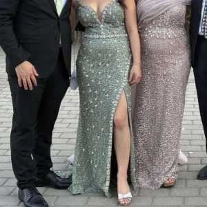 Glittrig grön långklänning med slits - Säljer en superfin långklänning i glittrande grönt med massor av paljetter och pärldetaljer. Klänningen har en hög slits framtill som ger en snygg och elegant look. Perfekt för bal eller festliga tillfällen när du vill sticka ut. Klänningen är insydd i midjan och längs vid läppen för att den inte ska gå sönder och då en mer elegant look 