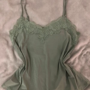 Grön linnetopp med spets från Amisu - Snygg ljusgrön linnetopp från Amisu i storlek XS. Toppen har tunna axelband och vacker spetsdetalj längs urringningen. Perfekt att styla med jeans eller kjol för en trendig look. Materialet känns mjukt och följsamt mot huden.