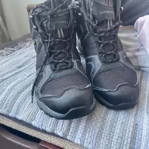 Svarta kängor från Bagheera med dubbar - Svarta kängor från Bagheera med HydroGuard-membran och grov sula med dubbar för extra grepp. Skorna har snörning, robust design och detaljer i syntet och textil. Perfekta för vinterns hala underlag och utomhusaktiviteter.