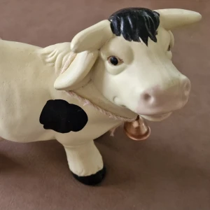 Prydnads kossa - Bilderna visar en dekorativ kofigur i keramik, målad i vitt med svarta fläckar och detaljer. Den har en liten bjällra runt halsen. Produkten har vissa små färgavskrap och märken, men är i överlag gott skick. Perfekt som prydnad eller samlarobjekt. Längd ca 18 cm och höjd ca 14 cm.