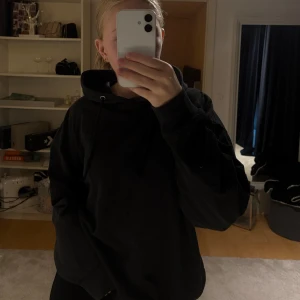 Svart oversized hoodie med huva - Säljer en svart oversized hoodie med huva och snörning. Tröjan har långa ärmar och en klassisk, enkel design utan tryck eller mönster. Perfekt för dig som gillar en chill och avslappnad stil.